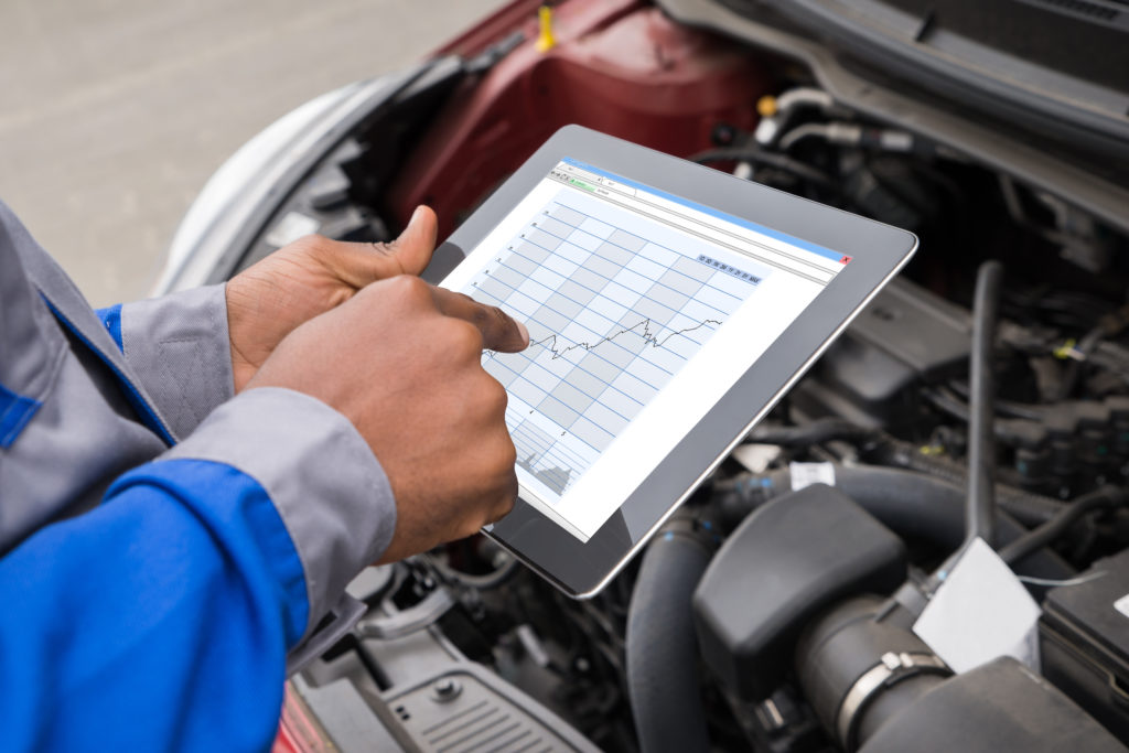 man using a tablet to do maintenance checks next to an open car engine