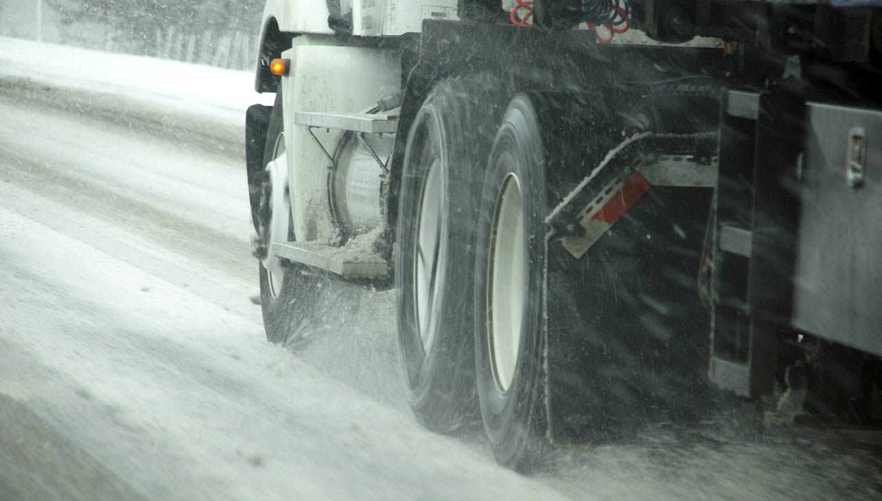 an hgv driving on a winter road with a lot of splash-back from the snow on the road