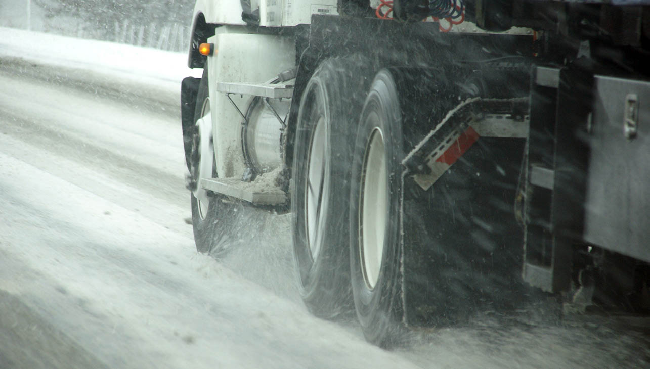 un vehículo pesado circulando por una carretera invernal con muchas salpicaduras de nieve en la carretera