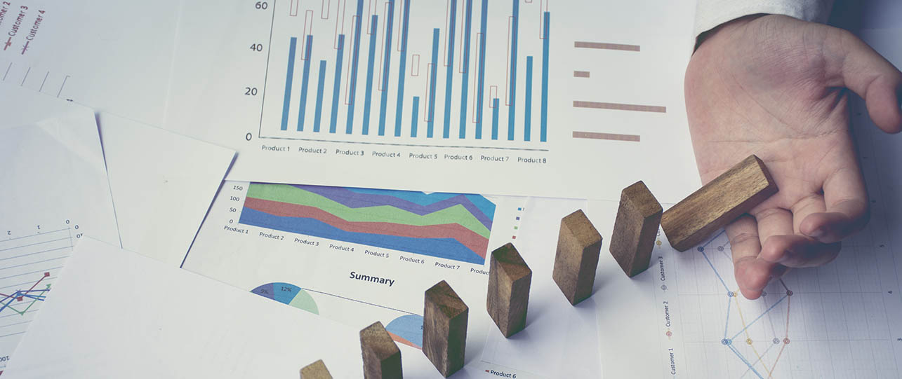 a man's hand with domino-like pieces all on top of an asset management plan which features graphs and data