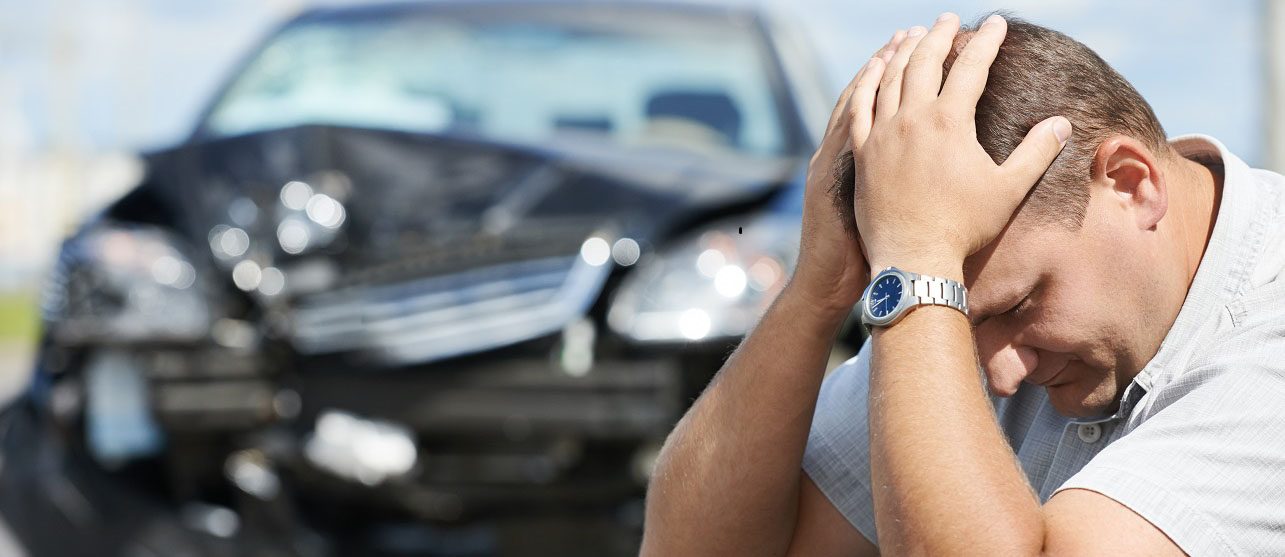 a man with his head in his hands with his smashed car in the background