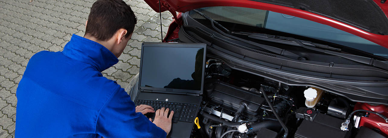 a technician using a laptop to perform the defect management process on this red vehicle