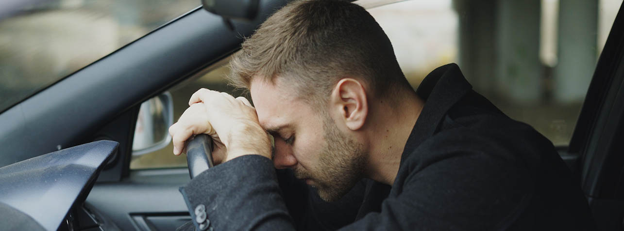 a man with a despaired look on his face leaning on a steering wheel