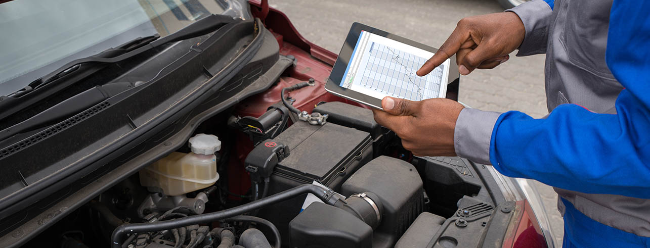 a technician in front of a car engine and using a tablet to achieve fleet compliance