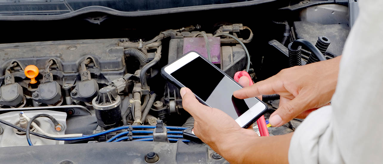 workshop manager checking a vehicle engine and holding a smartphone