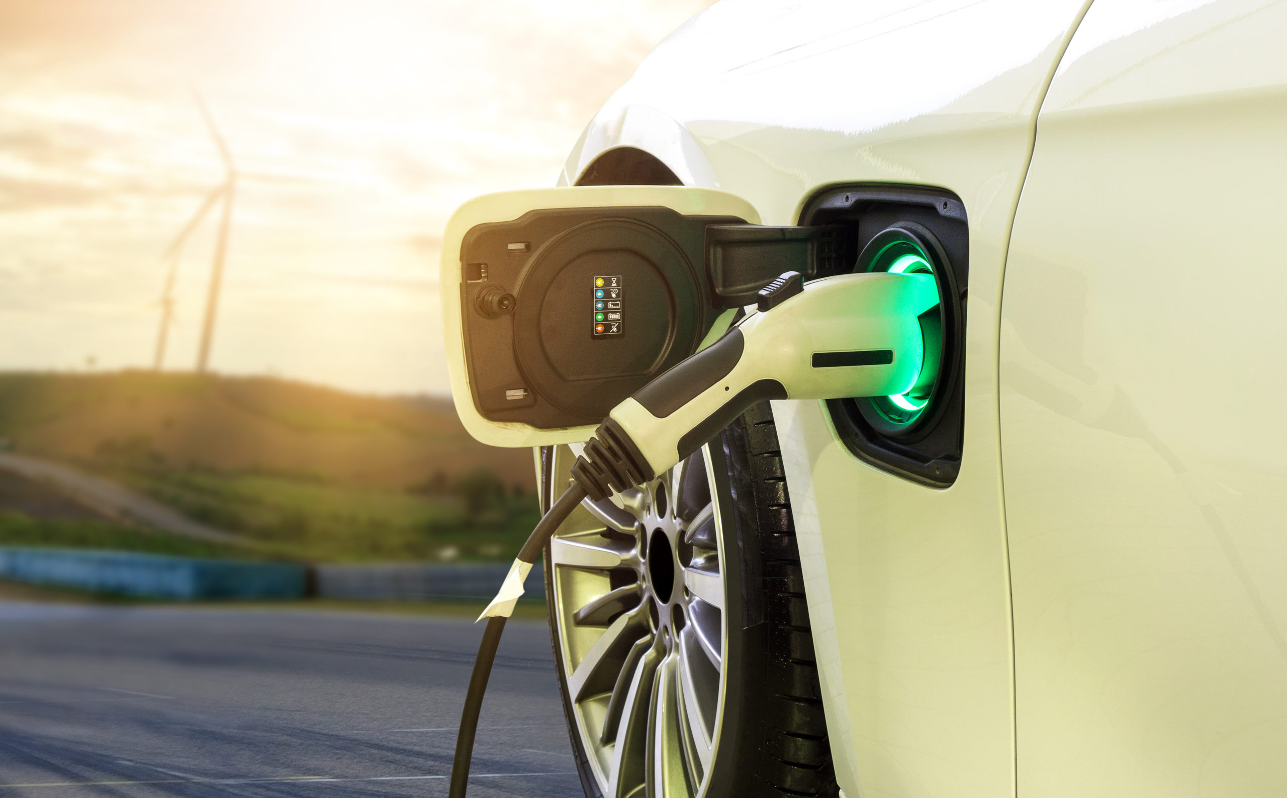 zero emissions vehicle being charged with wind turbines in the background