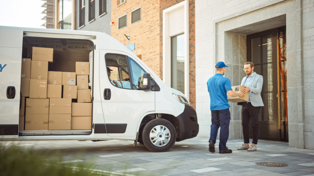 fleet driver delivering a parcel to a customer, with the delivery fleet vehicle parked behind him